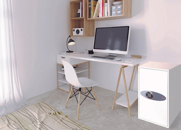 Compact gray home safe with digital keypad, placed on a wooden shelf under a book and small items.